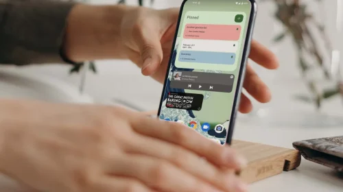 Hands placing an Android smartphone on a stand while the home screen and widgets are visible